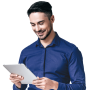 A smiling man with dark hair and a beard, wearing a blue button-up shirt, is looking at and holding a tablet with both hands.