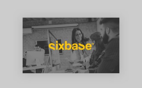 A group of people working together at computers in an office, with a woman standing and smiling at seated colleagues. The word sixbase in bold yellow text is centered over the image.