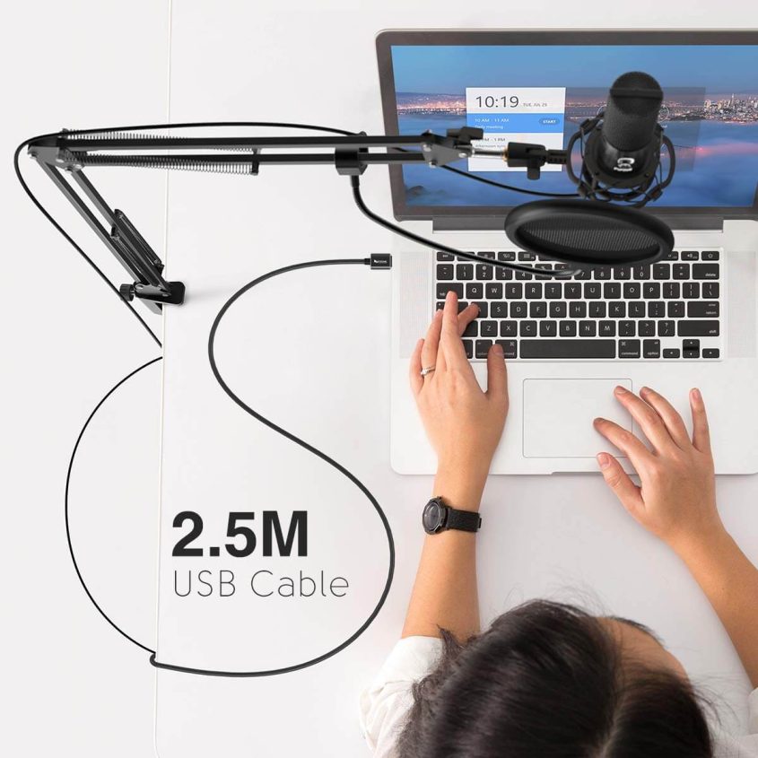 Person using a laptop with a mounted microphone, pop filter, and a 2.5-meter USB cable connected. The screen displays the time and date. The setup is organized on a white workspace.