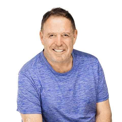 Smiling middle-aged man with short brown hair wearing a blue heathered t-shirt, sitting against a plain white background, ready for his appointment.