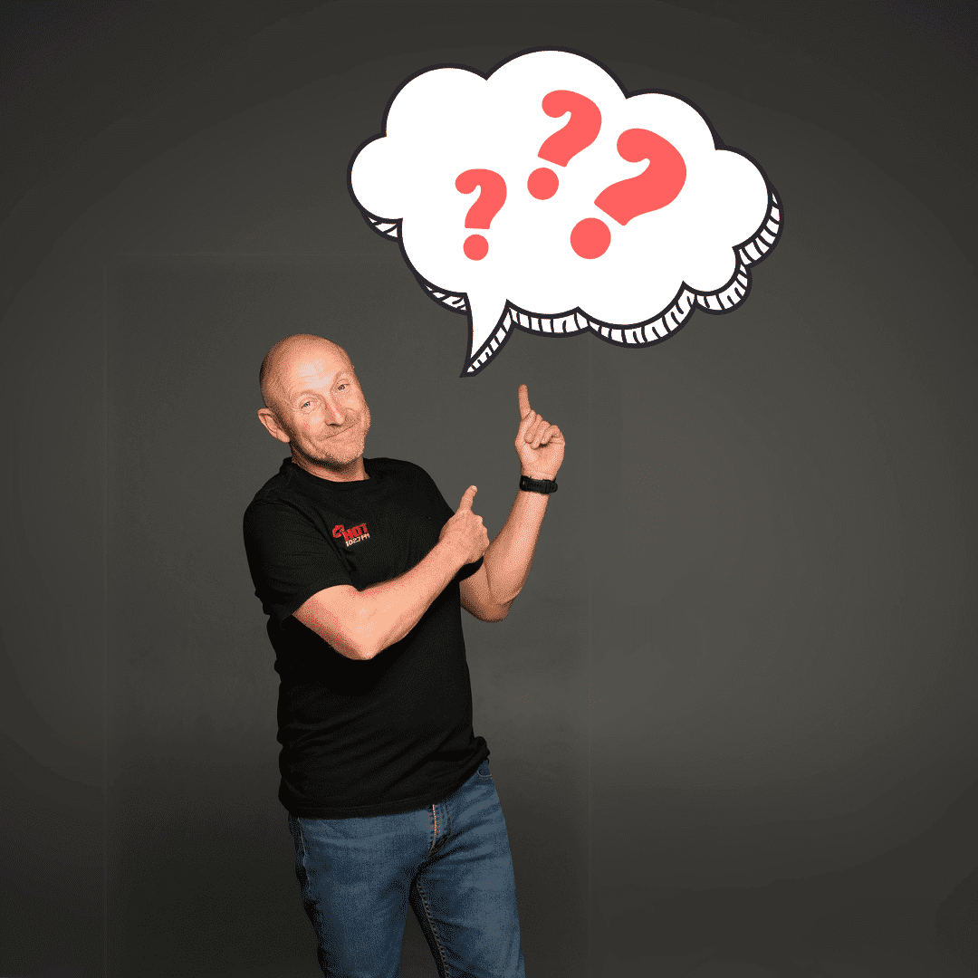 A middle-aged man in a black shirt and jeans stands, smiling and pointing upward at a large illustrated thought bubble filled with red question marks on a dark background.