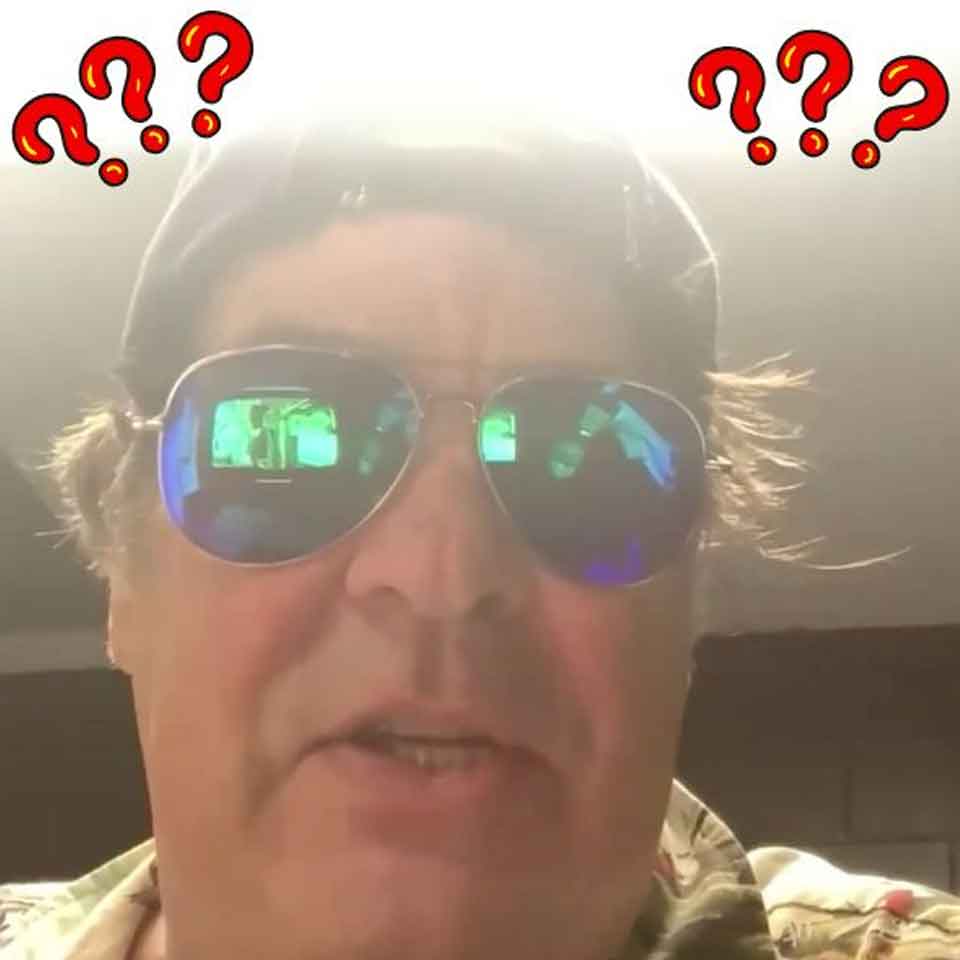 A man wearing a cap and reflective sunglasses looks at the camera with a confused expression. Red question marks surround his head. The background is dim, with bright light above his head.