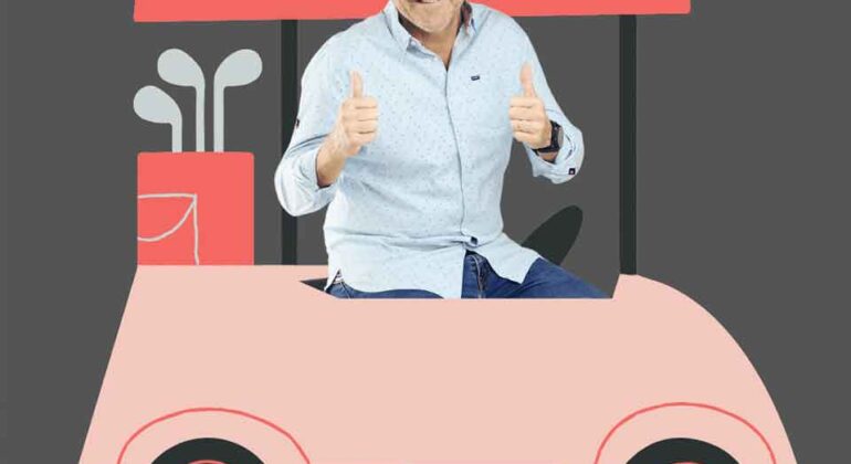A smiling bald man in a light blue shirt gives two thumbs up while sitting in a pink cartoon-style golf cart with golf clubs in the back, on a plain gray background.