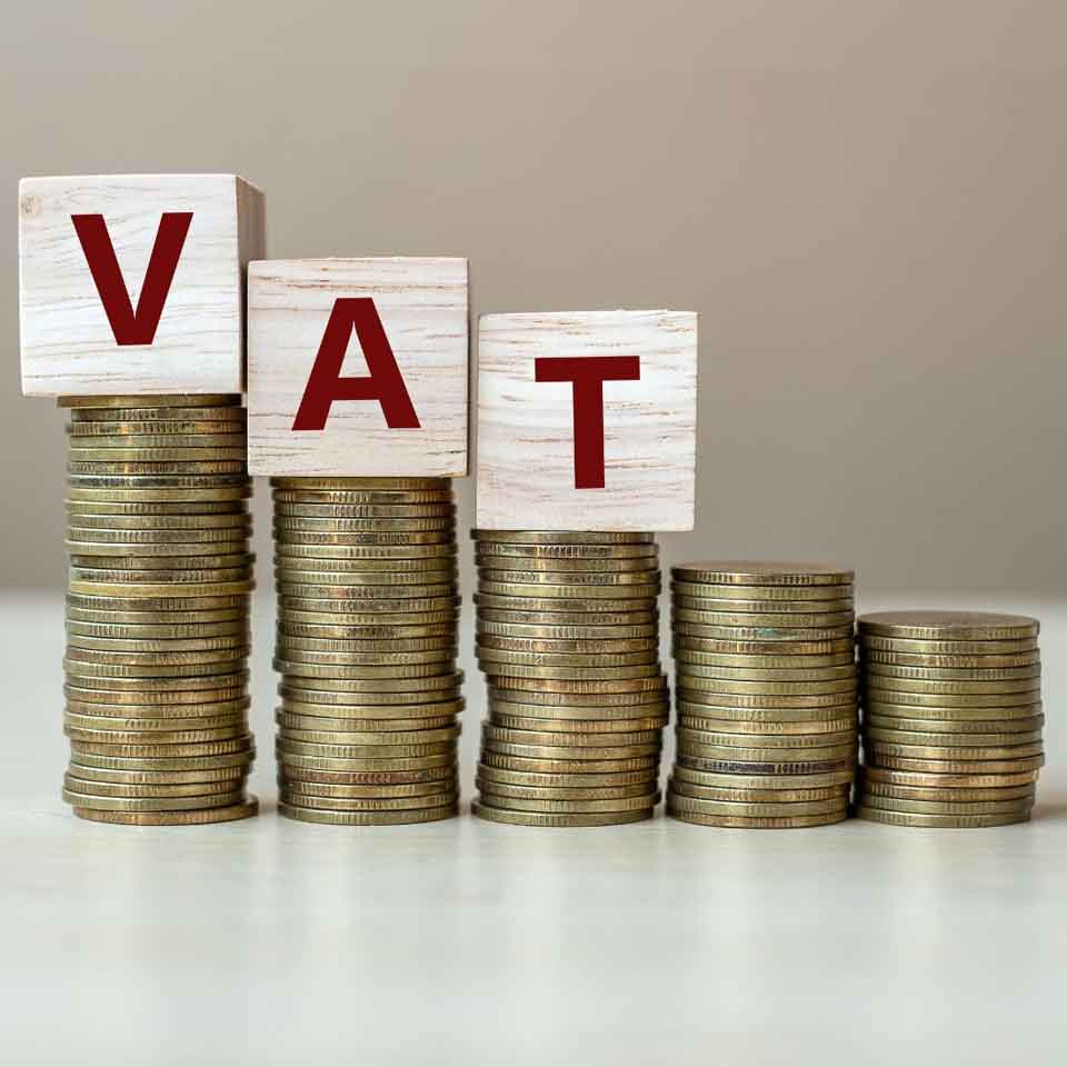 Stacks of coins increase in height from right to left, with wooden blocks on top spelling VAT in red letters, symbolizing value-added tax or financial growth.