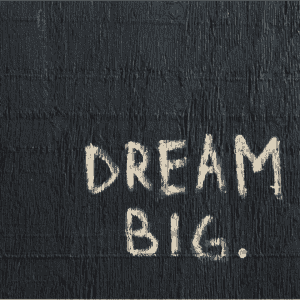 White painted text DREAM BIG. on a black textured wooden background.