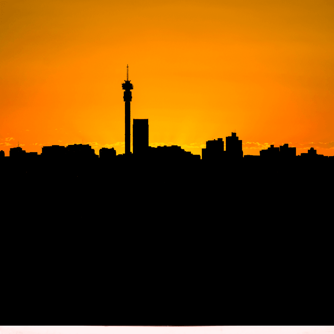 Silhouette of a city skyline at sunset, with an orange sky in the background and a tall communications tower standing prominently among the buildings.