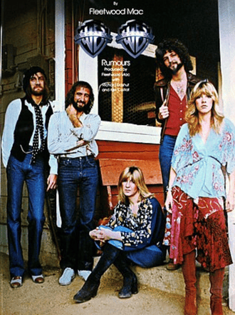 Five members of Fleetwood Mac pose outside a building; three stand and two sit on a step, all dressed in 1970s-style clothing. The iconic “Fleetwood Mac Rumours” album cover title appears above them.