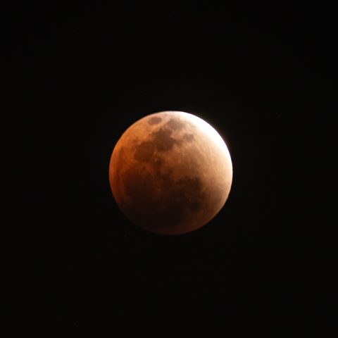 A Blood Moon is partially eclipsed by Earth's shadow against a dark night sky, with the upper right edge illuminated and the rest in shadow.