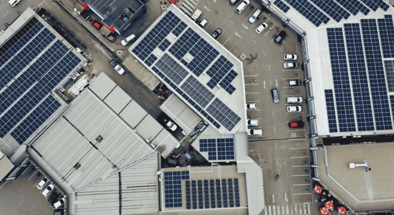 Aerial view of several large buildings with solar panels on their roofs and a parking lot filled with cars, highlighting new business opportunities in sustainable energy solutions.
