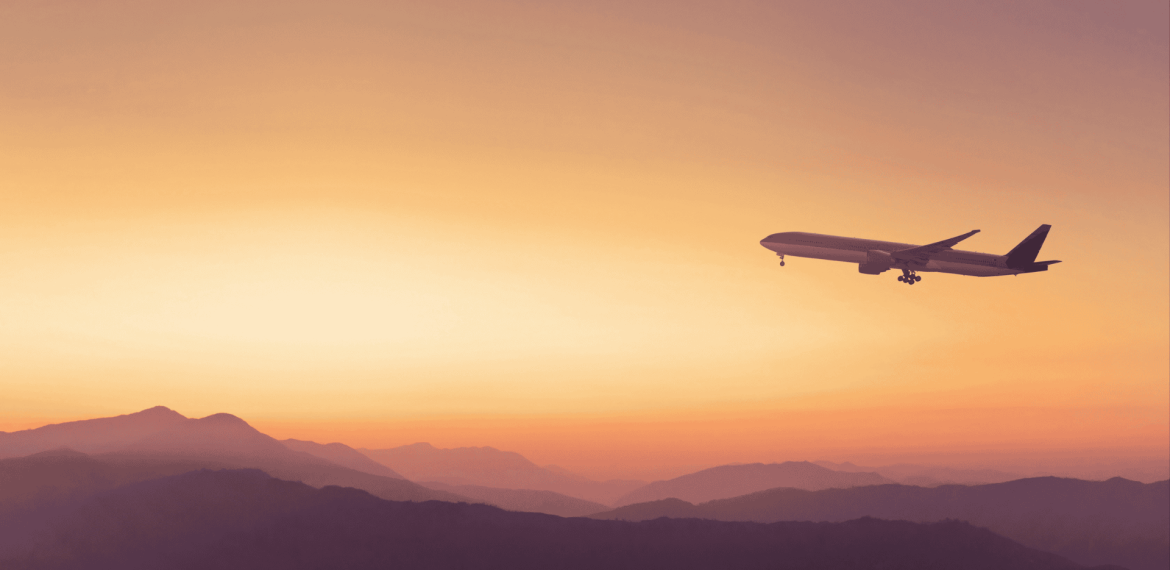 A commercial airplane flies above mountain silhouettes at sunset, with an orange and yellow sky in the background, symbolizing new business opportunities on the horizon.