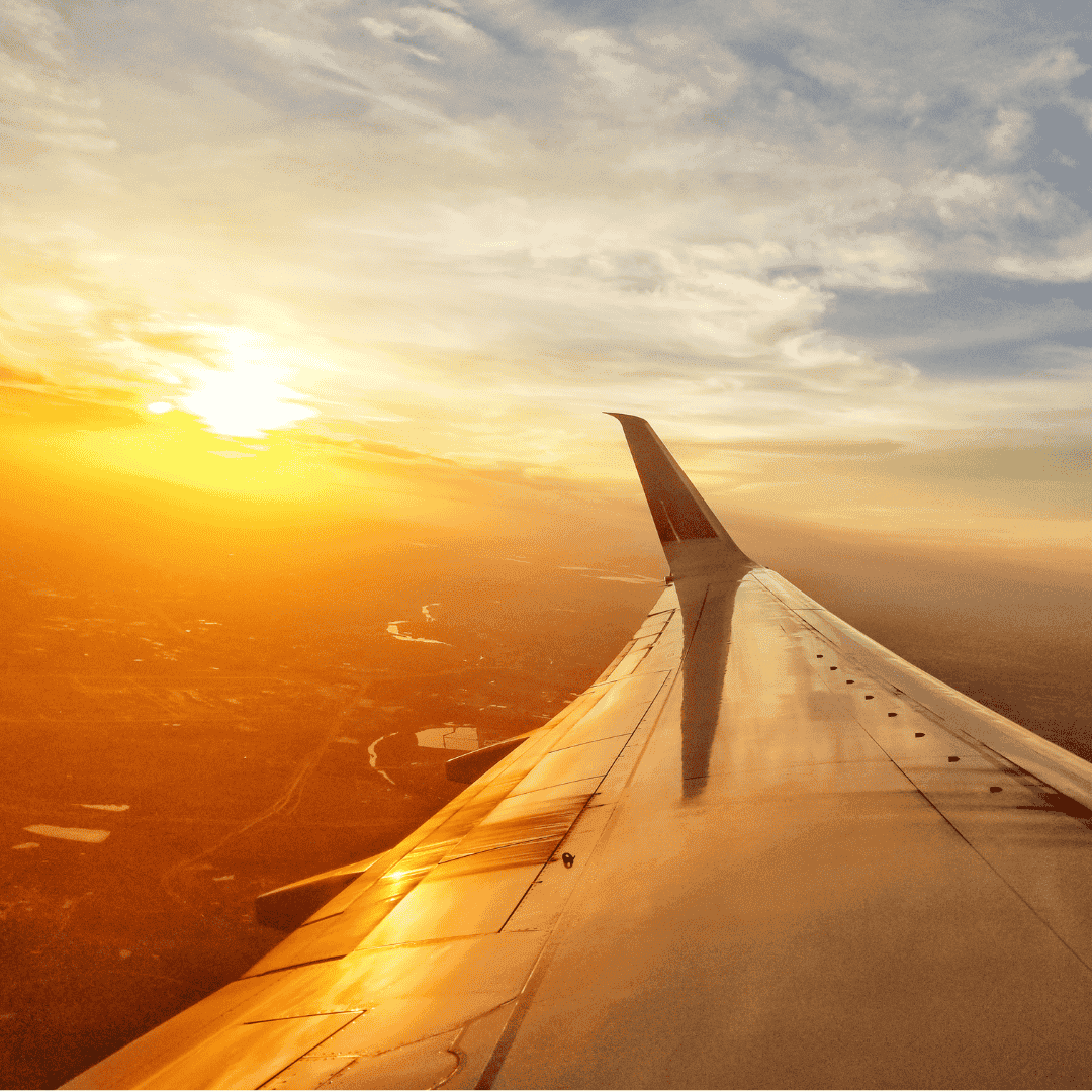 View from an airplane window showing the wing and engine in the foreground, with a golden sunset over scattered clouds—a reminder that new business opportunities await beyond every horizon.