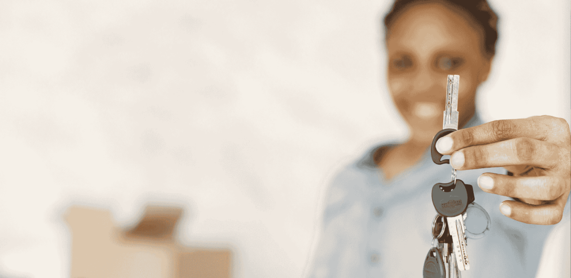 A person smiling and holding out a set of house keys, with moving boxes blurred in the background—symbolizing new beginnings and exciting business opportunities in real estate.
