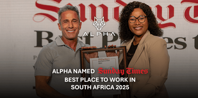 Two people stand smiling, holding a framed certificate. Behind them is an Alpha HOT Classic logo and a sign reading “Sunday Times Best Places.” Text below states: Alpha named Sunday Times Best Place to Work in South Africa 2025.