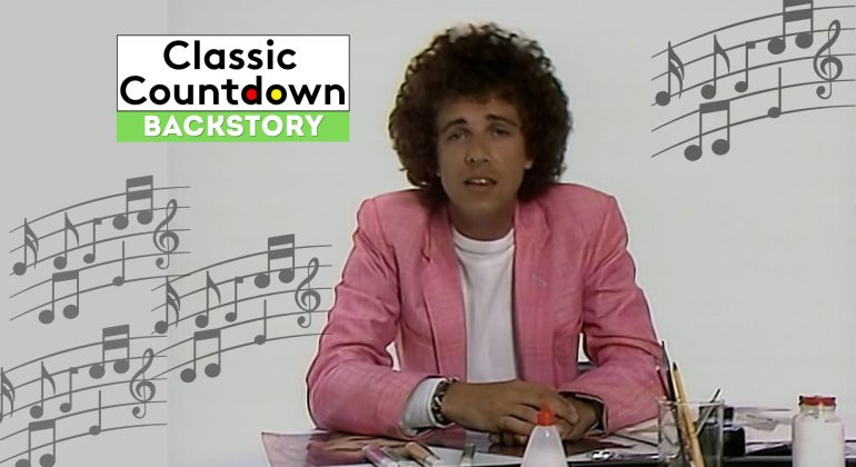 A man with curly hair in a pink blazer sits at a desk with papers and a glue bottle, channeling Prince vibes, with musical notes and the Classic Countdown Backstory logo in the background.