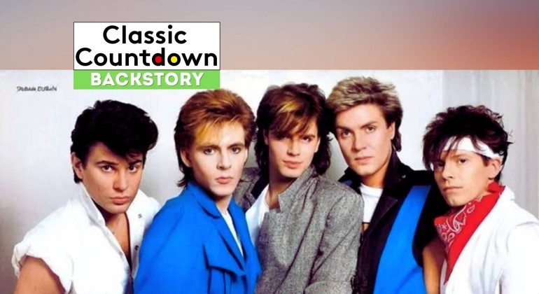 Five men with 1980s hairstyles and colorful outfits pose together against a light background. A banner at the top reads Classic Countdown Backstory, hinting at a nostalgic vibe reminiscent of hits like "Last Christmas.