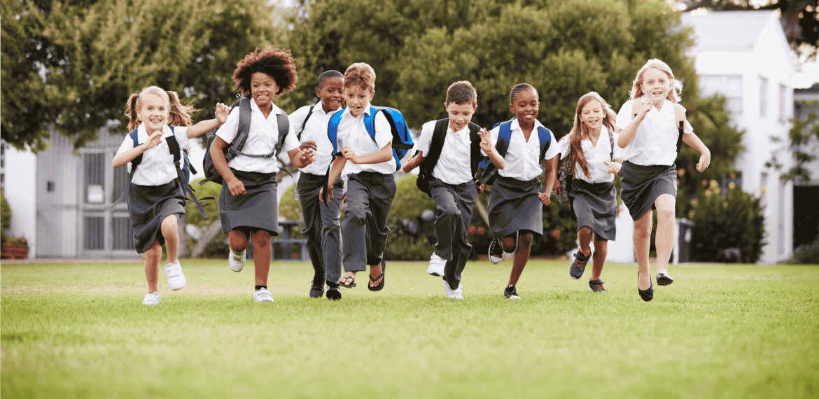 A diverse group of young children in school uniforms run happily across a grassy field, carrying backpacks, with trees and buildings—symbolizing future business opportunities—in the background.
