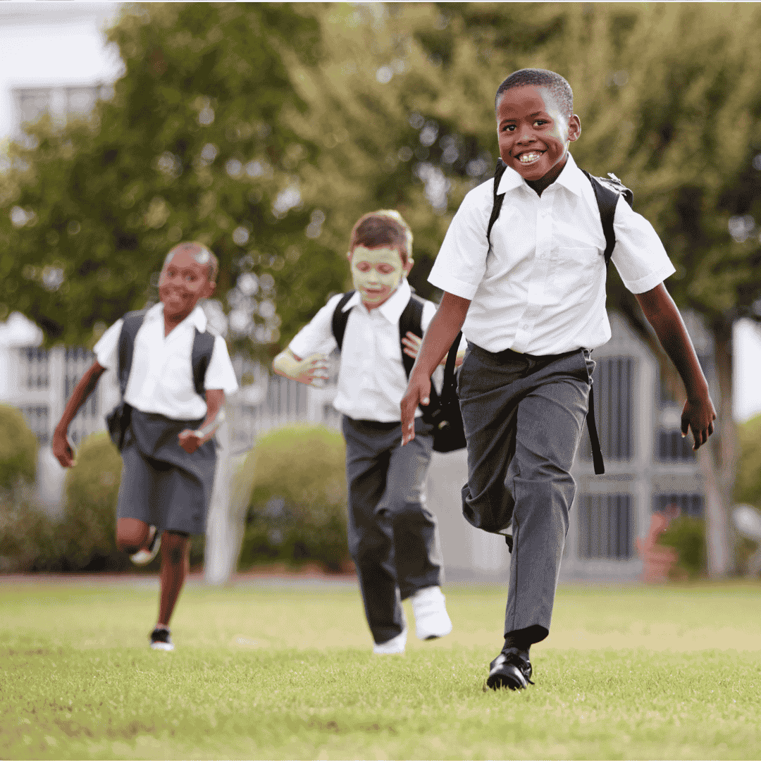 Three children in school uniforms with backpacks run and smile on a grassy field, full of energy and joy on their way to or from school—reminding us that education unlocks future business opportunities.