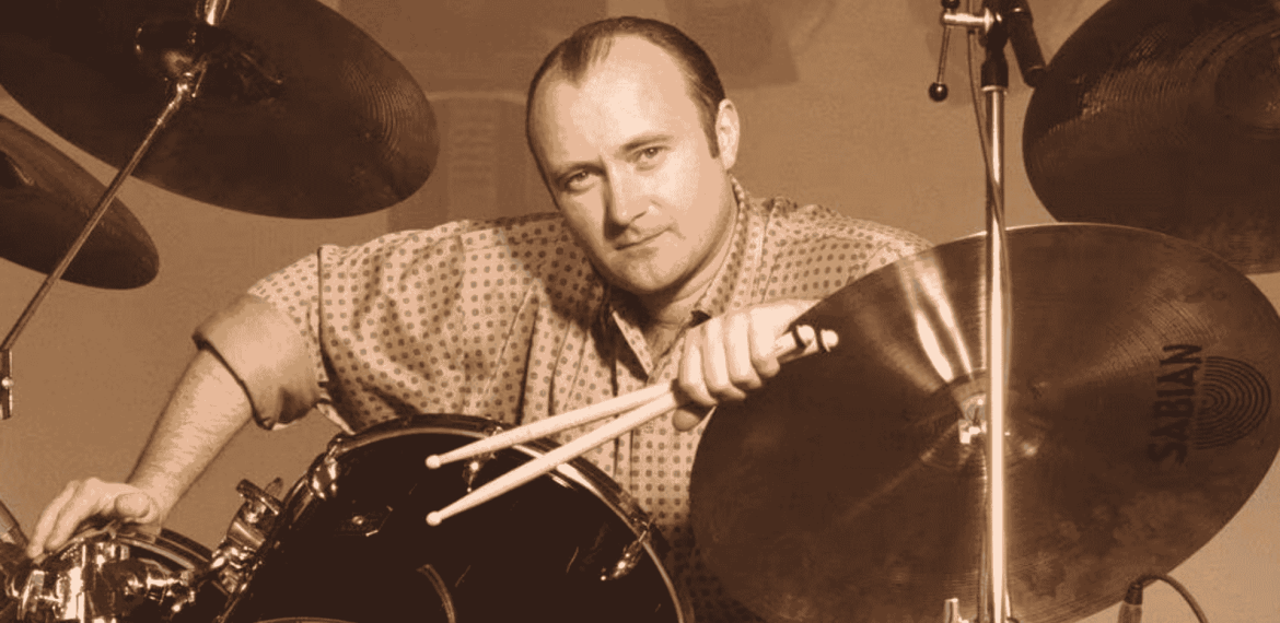 A man with a receding hairline and patterned shirt sits at a drum set, holding drumsticks and leaning on a Sabian cymbal, looking directly at the camera in a sepia tone—reminiscent of Phil Collins.
