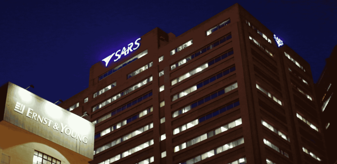 A nighttime view of two office buildings, one with a glowing ERNST & YOUNG sign and the other with a SARS sign near the top, their many lit windows shining like a Matric celebration against the dark sky.
