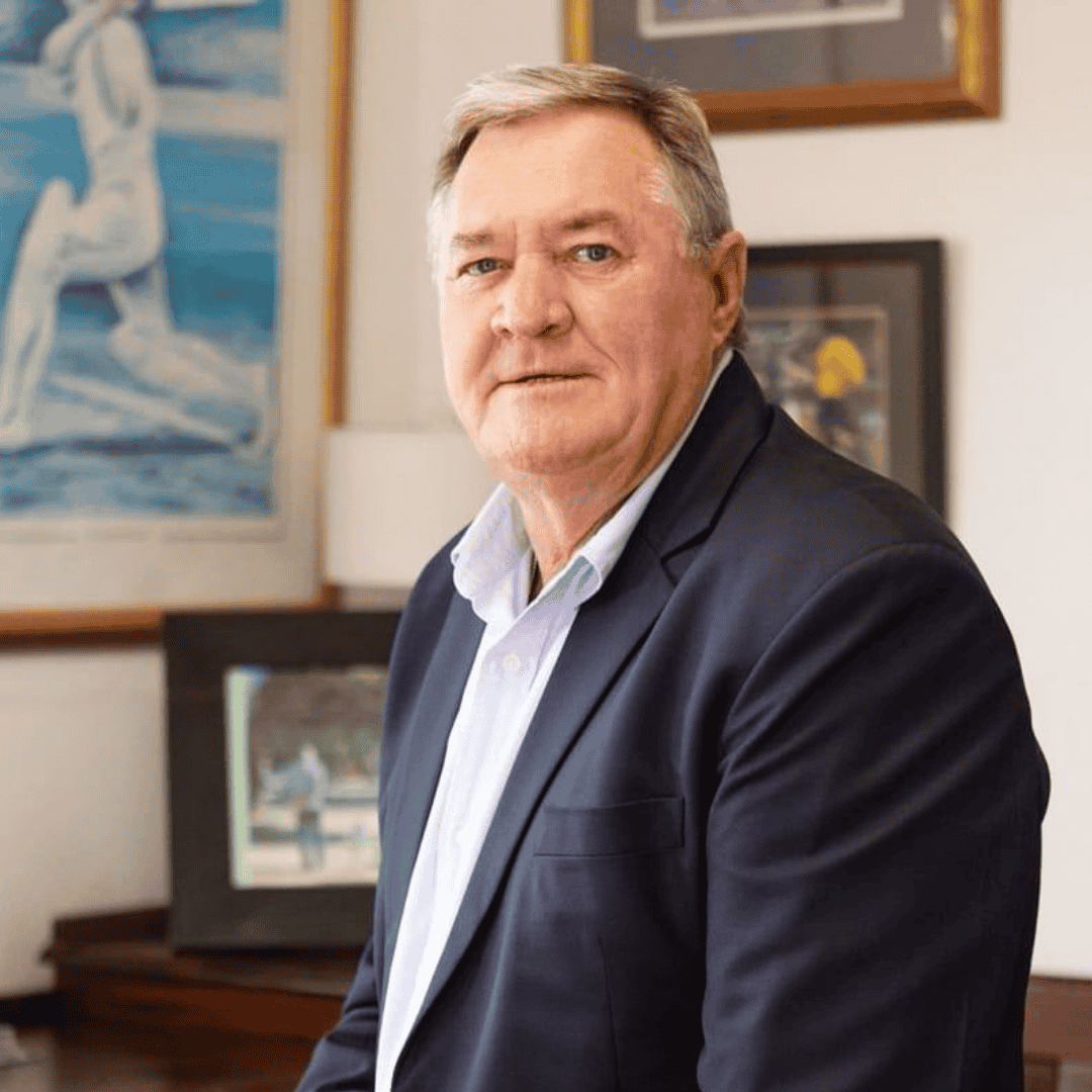 A middle-aged man with short gray hair, wearing a dark blazer and light shirt, sits indoors in front of framed artwork, smiling slightly at the camera—ready to share his thoughts on the Hot 1027 Breakfast show.