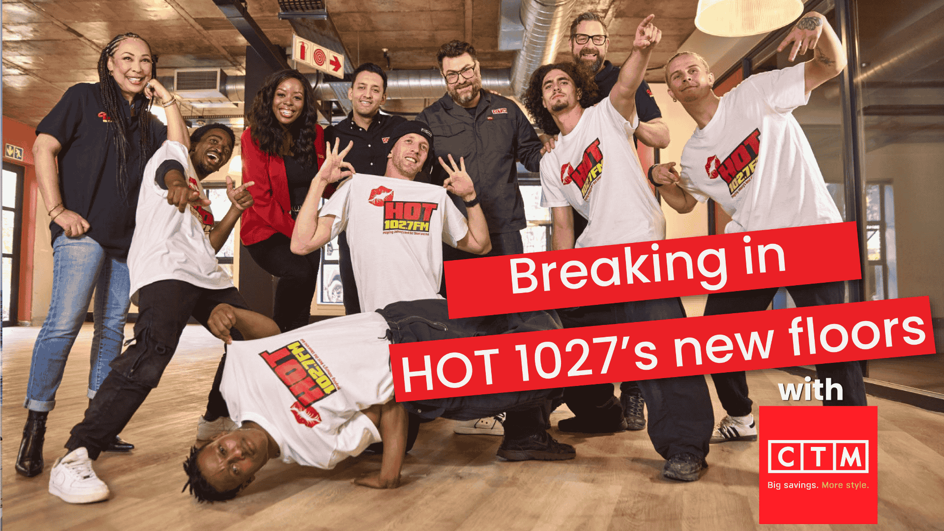 A group of people, some in HOT 102.7 FM shirts, pose playfully on a new wood floor. One person breakdances in front. Overlay text reads, Breaking in HOT 1027’s new floors with CTM.