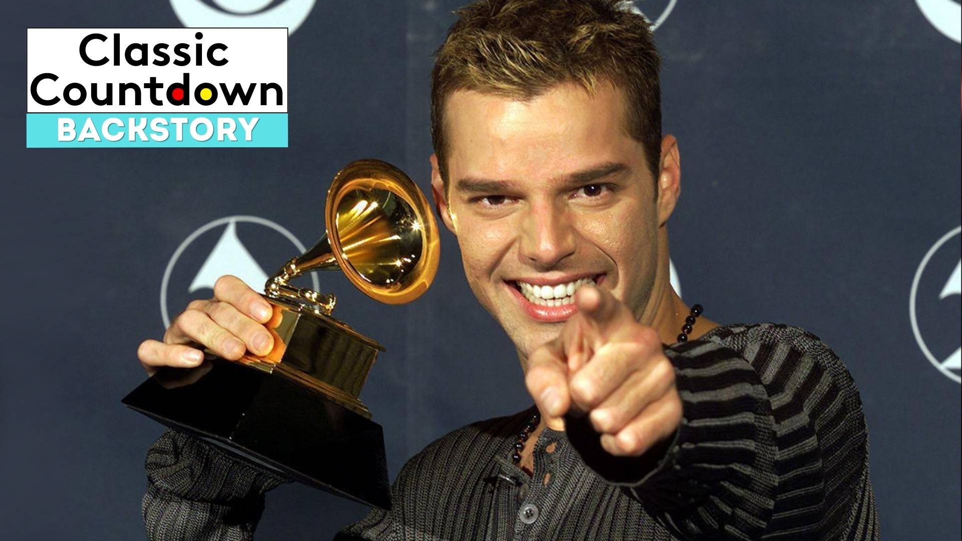 A smiling man holds up a Grammy award and points toward the camera. The background shows the Grammy logo, and a Classic Countdown Backstory graphic in the upper left corner highlights "Last Christmas.