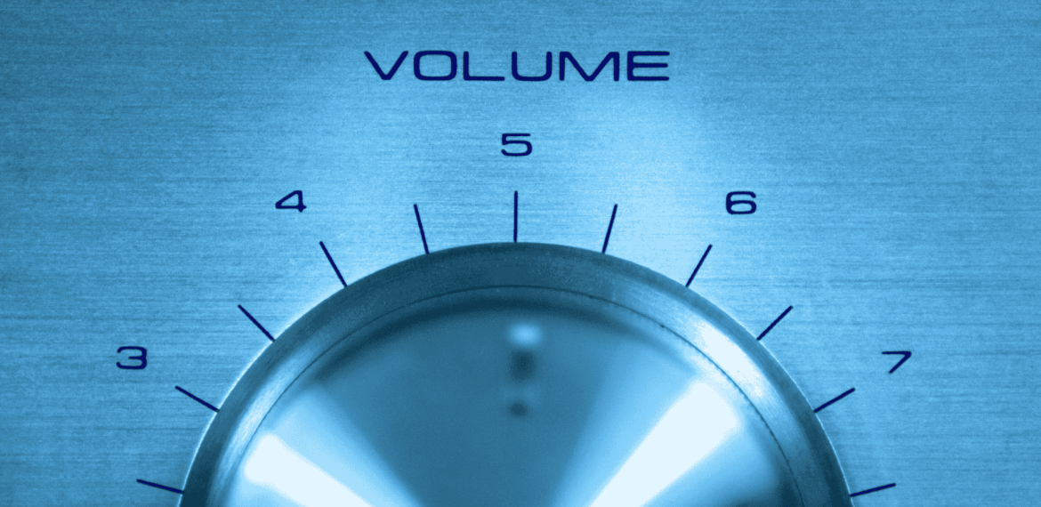 A close-up of a metallic volume control knob set between levels 5 and 6, with numbers 4 to 7 visible above the knob and "VOLUME" printed above in blue text. The blue-tinted image channels the early energy of a hot 1027 breakfast show.