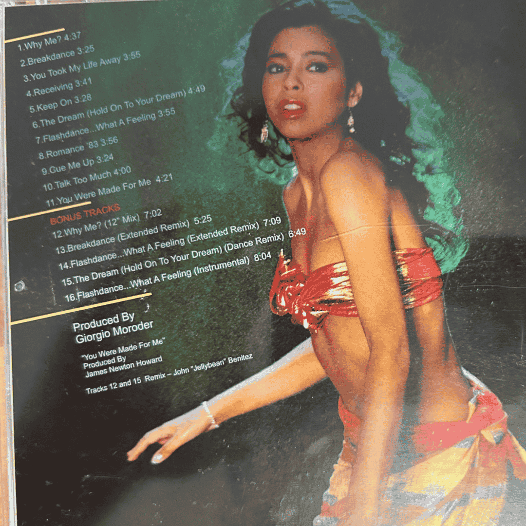 A woman in a red and gold outfit poses with one arm outstretched. To her left, the hot 1027 breakfast tracklist and production credits are printed in green and orange text on a black background.